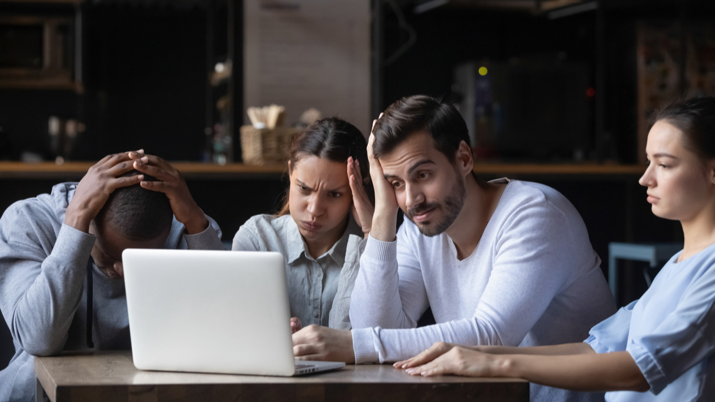 People gathered around a laptop on a desk looking very concerned